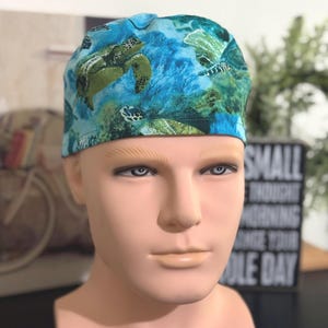 May include: A blue and green surgical scrub hat with a sea turtle pattern. The hat is made of a soft, comfortable fabric and is perfect for healthcare professionals.