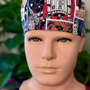 May include: A Star Wars themed surgical scrub cap. The cap features a comic book style design with images of R2-D2, Chewbacca, and other characters and elements from the Star Wars franchise. The background is a mix of black, red, and white.