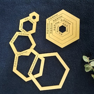 Könnte beinhalten: Satz von sechs sechseckigen Schablonen aus Holz mit Maßen in Millimetern. Die Schablonen sind ineinander verschachtelt, wobei die größte Schablone eine Außenkantenlänge von 55 mm und eine Innenkantenlänge von 45 mm hat. Die kleinste Schablone hat eine Außenkantenlänge von 15 mm und eine Innenkantenlänge von 10 mm.