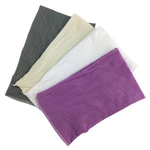 Puede incluir: Cuatro pa&ntilde;os de tela en diferentes colores: gris, beige, blanco y morado. Los pa&ntilde;os est&aacute;n doblados y apilados uno encima del otro.