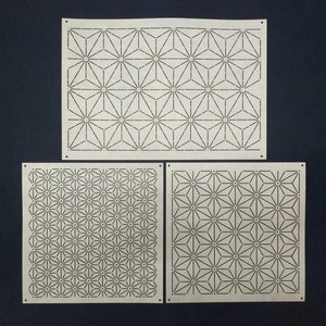 May include: Three white paper stencils with geometric patterns. The top stencil has a repeating pattern of six-pointed stars. The bottom two stencils have a repeating pattern of smaller six-pointed stars.