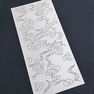 Könnte beinhalten: Eine weiße Papierschablone mit einem sich wiederholenden Muster aus stilisierten Wolken und Wirbeln. Die Schablone ist für die Verwendung mit Bastelarbeiten und DIY-Projekten konzipiert.