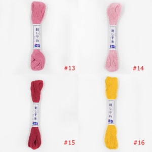 May include: Four skeins of embroidery floss in different colours: pink, light pink, red, and yellow. The skeins are labelled "刺し子糸" which translates to "Sashiko thread". The skeins are numbered 13, 14, 15, and 16.