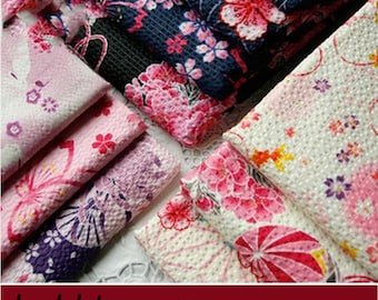 May include: Close-up of folded bubble cotton fabric in various floral patterns. The fabrics feature pink, red, and purple blossoms on backgrounds of white, pink, and navy blue. The text "bubble cotton" is visible at the bottom.