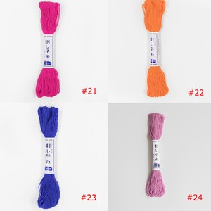 May include: Four skeins of embroidery floss in different colours: pink, orange, blue, and purple. Each skein has a white label with Japanese text and the number "刺し子糸" (Sashiko Ito) which means "Sashiko thread". The skeins are labelled with numbers 21, 22, 23, and 24.