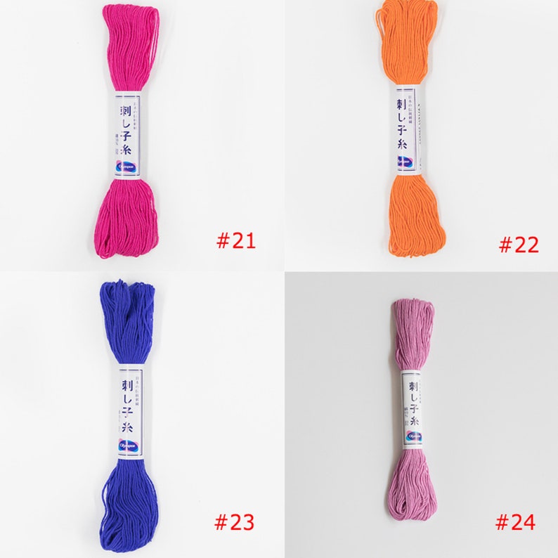 May include: Four skeins of embroidery floss in different colours: pink, orange, blue, and purple. Each skein has a white label with Japanese text and the number "刺し子糸" (Sashiko Ito) which means "Sashiko thread". The skeins are labelled with numbers 21, 22, 23, and 24.