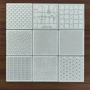 May include: Nine square stencils with diverse geometric and kitchen-themed designs. The stencils feature patterns like interlocking shapes, kitchen utensils, and puzzle pieces. The designs are in black lines on a white background.