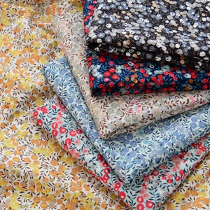 Peut inclure: Plusieurs échantillons de tissu à motifs floraux de différentes couleurs. Les tissus présentent de petits motifs de fleurs dans des tons de jaune, de rouge, de bleu et de noir. Les tissus sont empilés et pliés, présentant les différents motifs et couleurs.