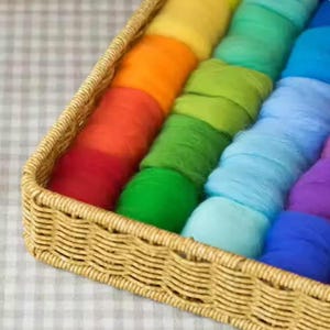May include: A rectangular woven wicker tray containing multiple rows of soft, colorful wool roving. The wool is arranged in a gradient of colors including red, orange, yellow, lime green, forest green, light blue, and deep blue.