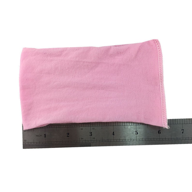 Puede incluir: Una diadema de tela rosa claro que mide aproximadamente 15 cm de largo. La diadema se muestra junto a una regla para referencia de tama&ntilde;o.
