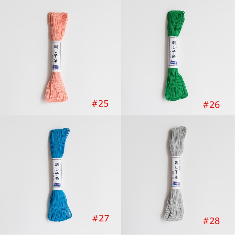 May include: Four spools of embroidery floss in different colours: peach, green, blue, and grey. Each spool has a white label with Japanese text and the number 25, 26, 27, or 28.