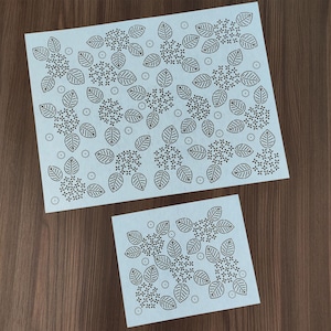 Puede incluir: Dos hojas de papel azul claro con un patrón repetido de hojas y elementos florales en marrón oscuro. La hoja más grande es rectangular y la más pequeña es cuadrada. El diseño presenta contornos de hojas detallados y pequeños grupos de flores.