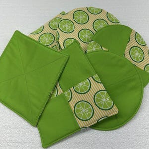May include: A collection of lime green and patterned kitchen textiles. The set includes square and circular items, with a lime slice pattern on a beige and white striped background. The solid items are a bright, vibrant green.