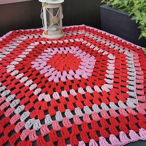Pode incluir: Um caminho de mesa de crochê com um design circular em tons de vermelho, rosa e cinza.