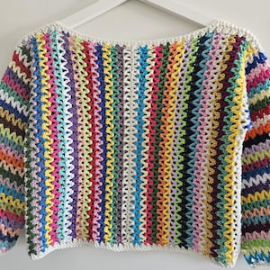 Op de afbeelding: Een kleurrijke, open gebreide gehaakte trui met een boothals. De trui heeft verticale strepen in verschillende kleuren, waaronder roze, geel, groen en blauw. De halslijn en manchetten zijn afgewerkt met een witte bies.