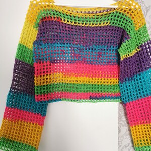 Op de afbeelding: Een regenboog-crochet top met lange mouwen. De top is gemaakt van een lichtgewicht, opengeweven stof met een kleurrijk gestreept patroon.