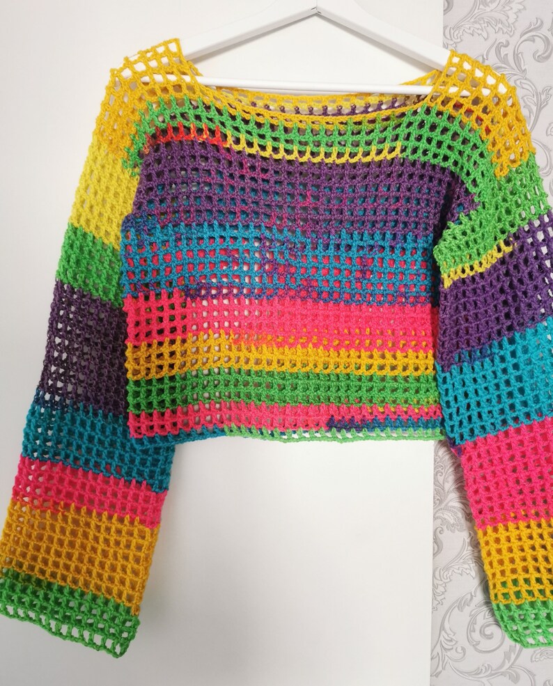 Op de afbeelding: Een regenboog-crochet top met lange mouwen. De top is gemaakt van een lichtgewicht, opengeweven stof met een kleurrijk gestreept patroon.