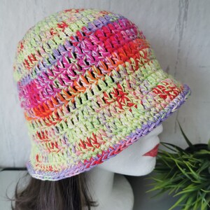 Könnte beinhalten: Ein bunter gehäkelter Bucket-Hut mit breiter Krempe. Der Hut ist aus verschiedenen Farben gefertigt, darunter Pink, Grün, Orange und Lila.