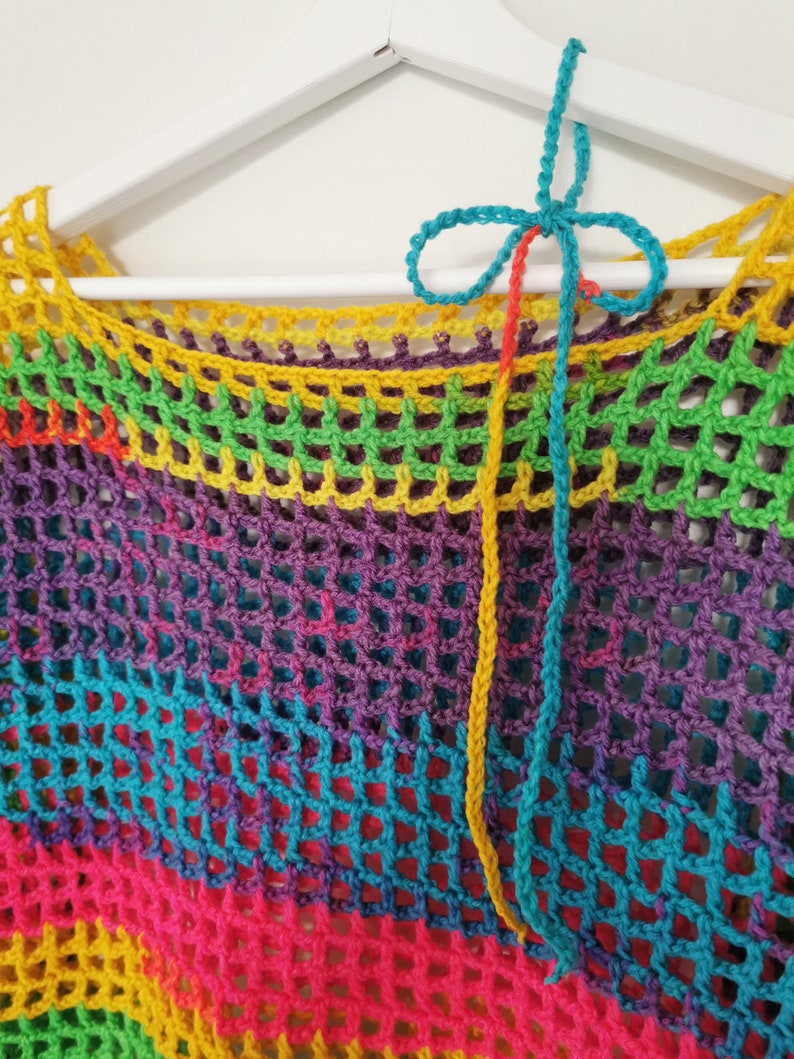 Op de afbeelding: Een regenboog gehaakt top met een kleurrijke gehaakte stropdas. De top is gemaakt met een gaaspatroon en heeft een losse pasvorm.