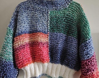 Op de afbeelding: Een handgemaakte trui met kleurblokken en een hoge halslijn. De trui heeft een patchwork-ontwerp met blauwe, groene, roze en rode secties. De manchetten en zoom zijn wit. De trui is gemaakt van een dik gebreid materiaal.