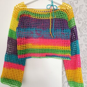 Op de afbeelding: Een regenboog gestreept gebreid topje met lange mouwen. Het topje is gemaakt van een los, open weefsel en heeft een verkorte lengte.