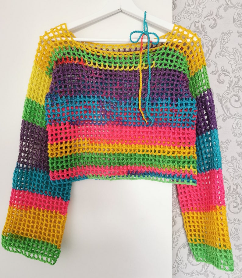 Op de afbeelding: Een regenboog gestreept gebreid topje met lange mouwen. Het topje is gemaakt van een los, open weefsel en heeft een verkorte lengte.