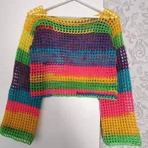 Op de afbeelding: Een regenboog gestreept gebreid topje met lange mouwen. Het topje is gemaakt van een losse, open geweven stof.