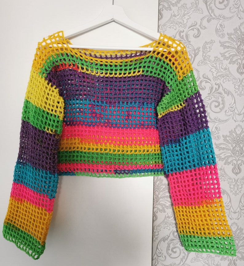 Op de afbeelding: Een regenboog-crochet top met lange mouwen en een losse pasvorm. De top is gemaakt van een lichtgewicht, ademend materiaal en heeft een kleurrijk gestreept patroon.