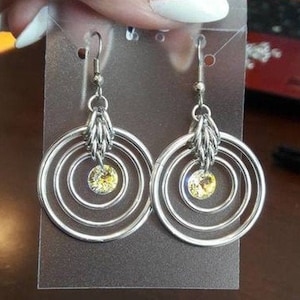 Puede incluir: Pendientes de aro de plata con múltiples círculos concéntricos y un cristal amarillo en el centro.