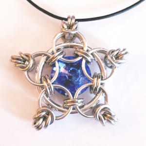May include: A silver star-shaped pendant with a blue crystal in the center. The pendant is attached to a black cord.