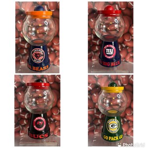 May include: Four glass candy jars with team logos painted on the bases. The jars are decorated with the logos of the Chicago Bears, New York Giants, Tampa Bay Buccaneers, and Green Bay Packers. The jars are all on a white background.