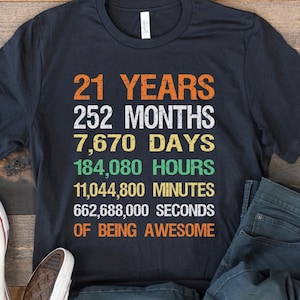 May include: Black t-shirt with white text that reads "21 Years, 252 Months, 7,670 Days, 184,080 Hours, 11,044,800 Minutes, 662,688,000 Seconds of Being Awesome".