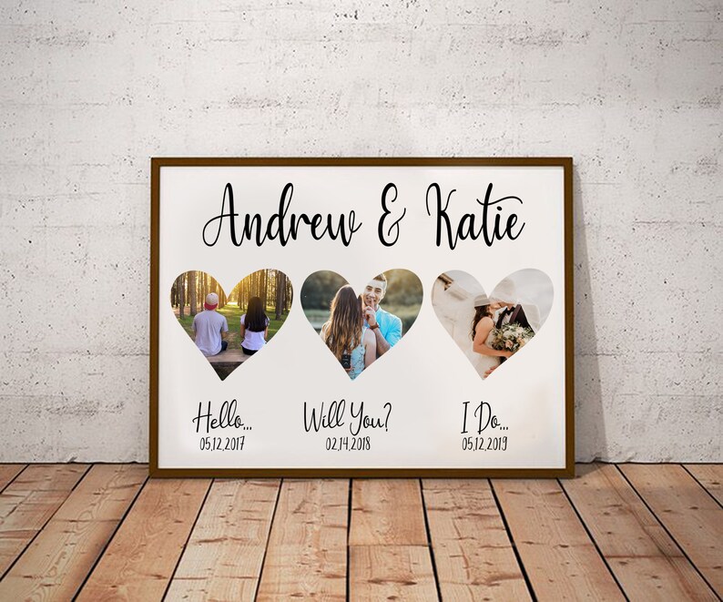 K&ouml;nnte beinhalten: Gerahmter Druck mit drei herzf&ouml;rmigen Ausschnitten, die jeweils ein Foto enthalten. Oben auf dem Rahmen steht "Andrew & Katie" in Schreibschrift. Unter den Fotos stehen die S&auml;tze "Hello...", "Will You?" und "I Do..." mit Daten.