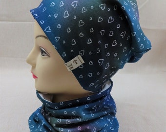 May include: A blue and purple beanie and neck gaiter with a white heart pattern. The beanie has a fold-over design and the neck gaiter is a tube shape.