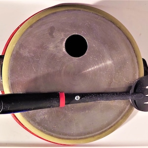 May include: A black and red spatula with a hole in the center, resting on top of a round, silver pan with a yellow rim.
