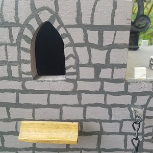 May include: A gray wooden castle with two arched windows and a small wooden ledge. The castle is painted to look like stone with gray mortar.