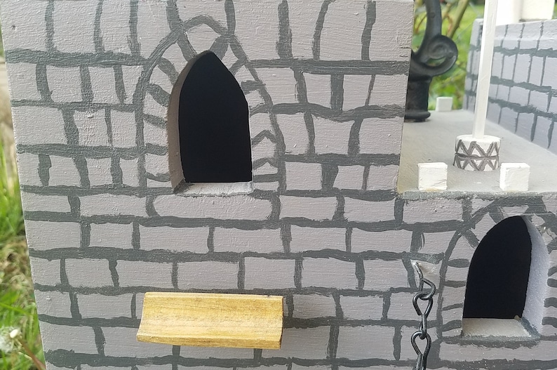 May include: A gray wooden castle with two arched windows and a small wooden ledge. The castle is painted to look like stone with gray mortar.