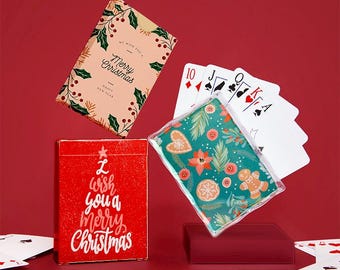 May include: Two decks of playing cards with Christmas-themed designs. One deck has a red background with the text "I wish you a merry Christmas". The other deck has a green background with a gingerbread man and floral designs.