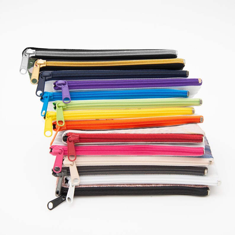 May include: A stack of 12 colorful zippered pouches with different patterns and colors. The pouches are made of fabric and have a zipper closure. The pouches are stacked on top of each other, with the top pouch being black and the bottom pouch being white.