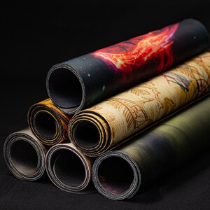 Op de afbeelding: Vijf opgerolde speelmatten met verschillende kleurrijke ontwerpen. De matten zijn opgerold en op elkaar gestapeld. De matten zijn gemaakt van een zacht, duurzaam materiaal en perfect voor tabletop gaming.