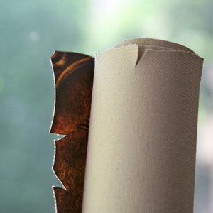 Pu&ograve; includere: Un primo piano di un dipinto su tela arrotolato con una cornice marrone e dorata. La tela &egrave; bianca e la cornice &egrave; parzialmente visibile.