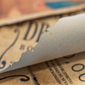 May include: Close-up of a rolled up piece of paper with the word "DR" visible. The paper is beige and has a rough texture. The paper is rolled up and the edges are frayed.