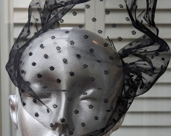 May include: A black polka dot veil made of sheer fabric. The veil is draped over a mannequin's head.