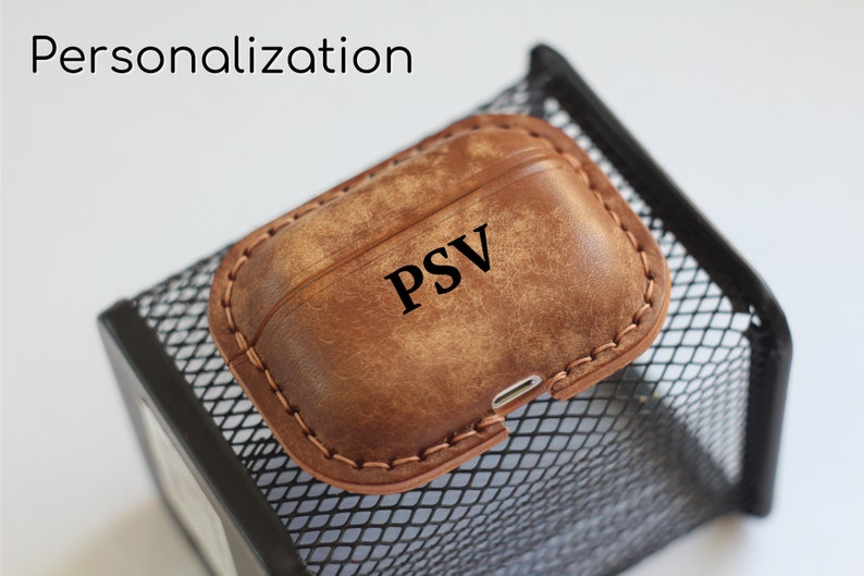 May include: A brown leather case for AirPods with the initials "PSV" embossed on the front.