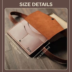 May include: A handmade leather bag with a strap, featuring a light brown interior and a darker brown exterior. The bag is 19 cm long and 10.5 cm wide. The name "Sara" is visible on the front.