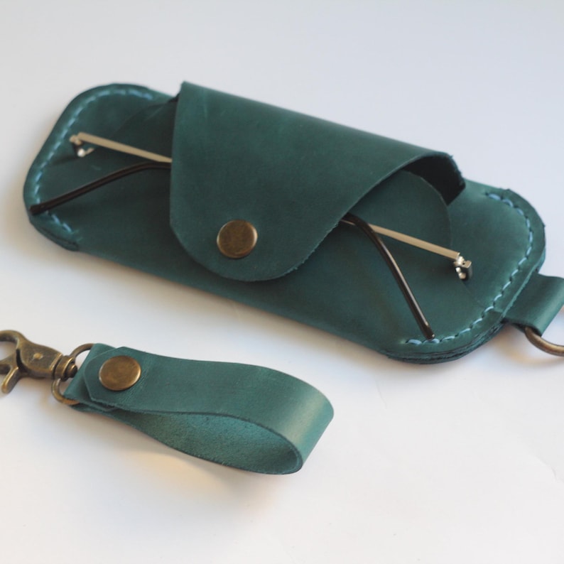 May include: A teal leather glasses case with a snap closure and a matching teal leather keychain with a metal clasp.