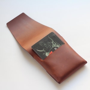 May include: A brown leather card holder with a card partially visible inside. The card has a black background with a white and red design. The card holder is open, showing the interior.