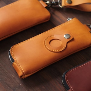 Peut inclure: Gros plan sur plusieurs étuis à clés en cuir de différentes nuances de marron. Les étuis à clés ont une fermeture éclair et un accent circulaire avec un bouton-pression. Le cuir est cousu avec un fil contrastant, et certains ont une dragonne.