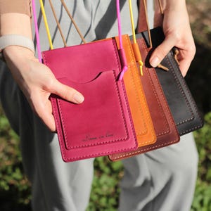 May include: Five leather phone cases in different colors, including burgundy, orange, brown, and black. The burgundy case has the text "Love in Love" embossed on the front.