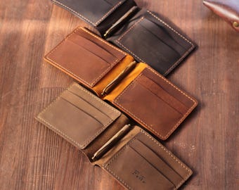 May include: Four open leather wallets in various shades of brown, showcasing card slots and money clips. The wallets are arranged on a wooden surface, with visible stitching and a personalized initial on one wallet.